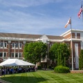 Peoplegatherunderawhiteeventtentonthelawnofared-brickmedicalschoolbuildingwithflagsflyingintheforeground