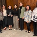 Agroupofwomenposetogetherindoorsoneholdinganawardsmilingincelebrationofaprofessionalrecognition