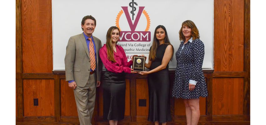Two students and two faculty members at VCOM-Virginia stand together during an award presentation ceremony.