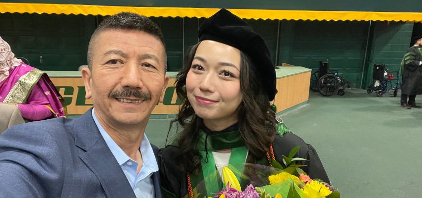 A medical graduate poses in regalia with a man holding the camera for a celebratory selfie at commencement.