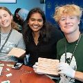 Threestudentsinaclassroomsettingsmileandholdupsuturepracticepadsduringahands-onmedicaltrainingactivity
