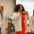 Astudentinareddressputsonawhitecoatduringawhitecoatceremonywhileothersonstagelookon