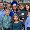 Agraduateinabluecapandgownholdsadiplomawhilesurroundedbysmilingfamilymembersoutsidetheceremonyvenue