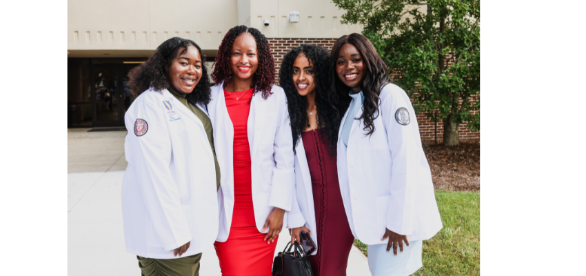 Four women stand smiling outside donning their new white coats.