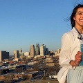 AsmilingmedicalstudentinawhitecoatholdsaMatchedsigninfrontofacityskyline