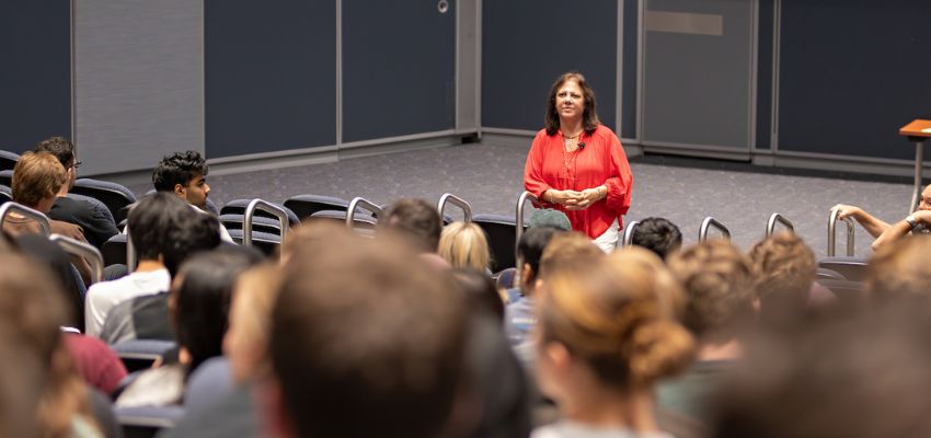 A woman stands at the front of the lecture hall, addressing a room of engaged medical students