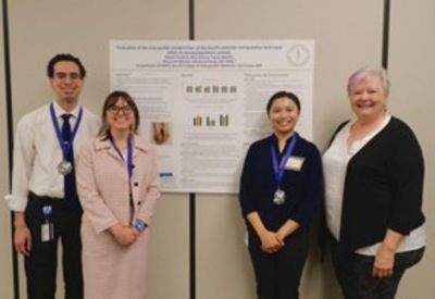 Three students wearing medals and a faculty member stand in front of a research poster, smiling for the photo.