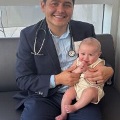 Amedicalstudentwearingastethoscopeandsuitsmileswhileholdingababyonhislap