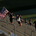 AgroupofpeoplewalkupstadiumstepsatsunriseonecarryingalargeAmericanflag