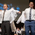 Studentsputonwhitecoatsonstageduringaceremonywithanaudienceseatedbehindthem