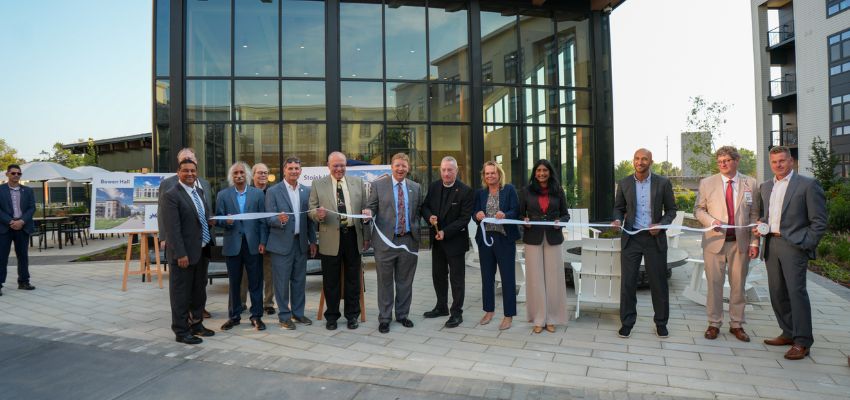 A group of leaders and faculty cut a ribbon in front of a glass building during a ribbon-cutting ceremony.