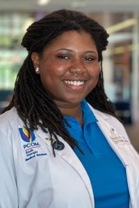 Portrait of a woman in a white coat with a PCOM South Georgia logo on her shirt, smiling indoors.