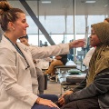 Amedicalstudentinawhitecoatusesaneyecharttoexamineayoungpatientwearingaheadscarfinaclinicaltrainingsetting