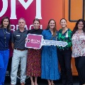 AgroupofpeoplestandinfrontofaVCOMmobilemedicaloutreachvehicleholdingalargeceremonialkeyandsmilingforthephoto