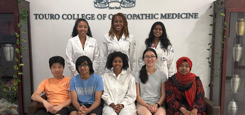 Group of students and faculty pose for a photo at Touro College of Osteopathic Medicine, with some wearing white coats and others casual clothing.