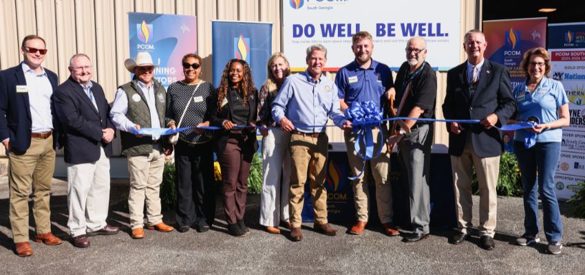 Group of people stand in front of a PCOM South Georgia sign and banners during a ribbon-cutting ceremony, smiling for the photo.