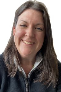 Headshot of a woman smiling, wearing a black zip-up sweater over a white shirt, with a light background.