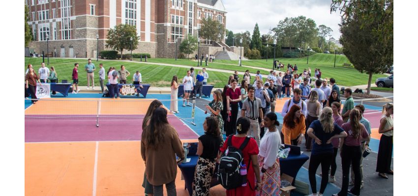Students gather outdoors around tables on colorful courts during a campus event.