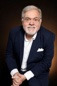 A man in a suit poses for a professional portrait against a dark background.