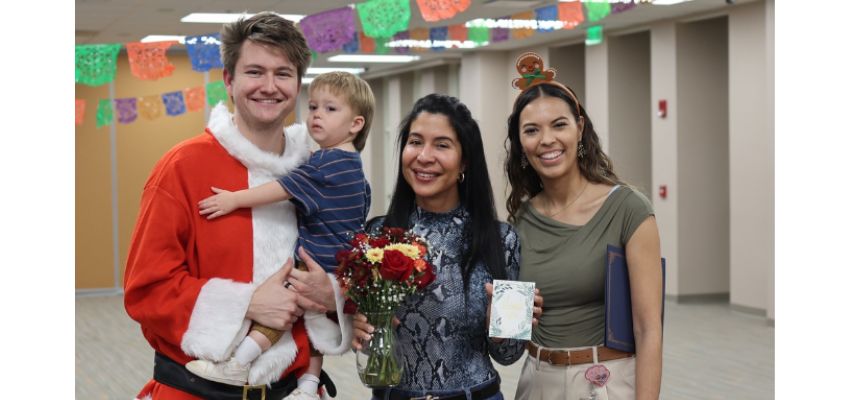 Four people, including a child, smile together indoors during a festive gathering with colorful decorations overhead.