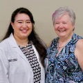 Awomaninawhitecoatstandsnexttoanotherwomaninapatternedblousebothsmilingatthecamera