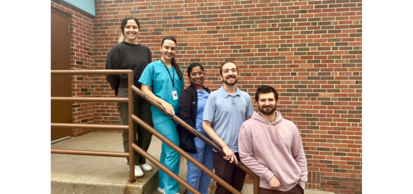 A group of five individuals, including medical professionals in scrubs, pose together on a staircase outside a brick building.
