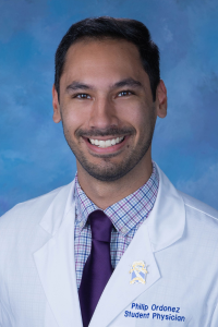 Philip smiles for a professional headshot, wearing his white coat