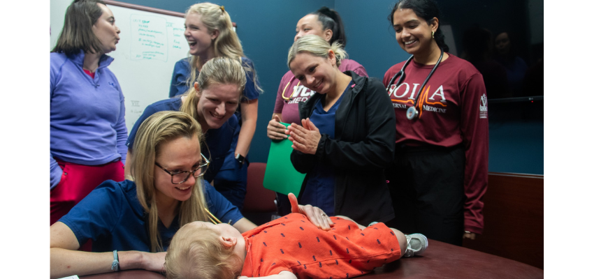 Students giggling with baby on exam table