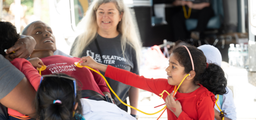 Little girl places stethoscope on medical manikin