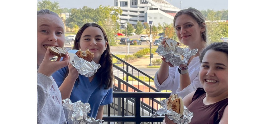 Students stand on balcony while eating bagels