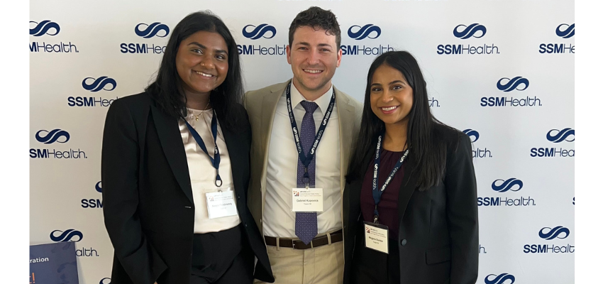 Three students stand in front of SSMHealth step and repeat