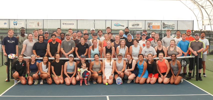 Dozens of students lined together on a pickleball court.