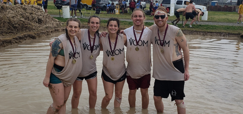 Five students pose with medals in muddy water