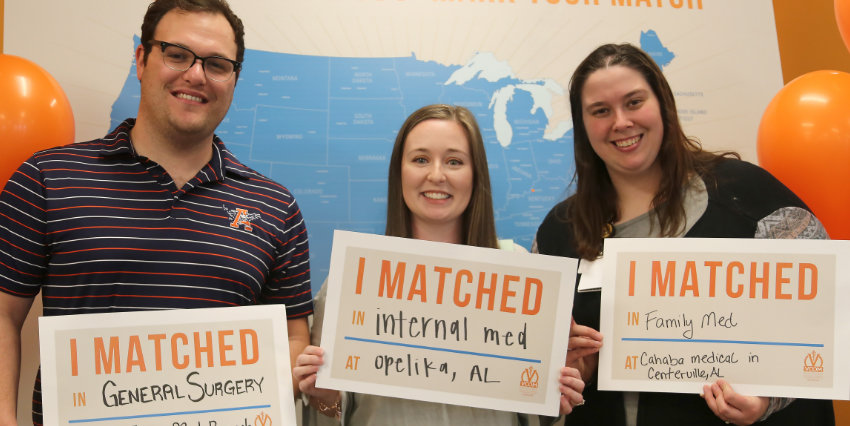 Three smiling med students facing the camera and holding 