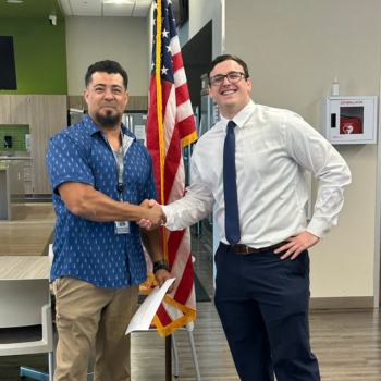 Professor and student shake hands in front of American flag