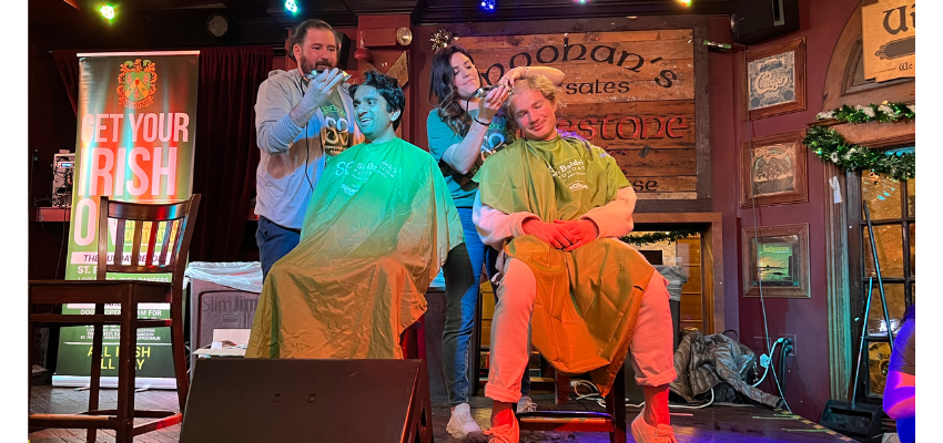 Two students having their heads shaved on stage