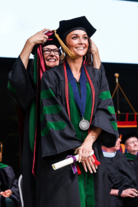 graduate in a cap and gown receiving their diploma on stage during a commencement ceremony.