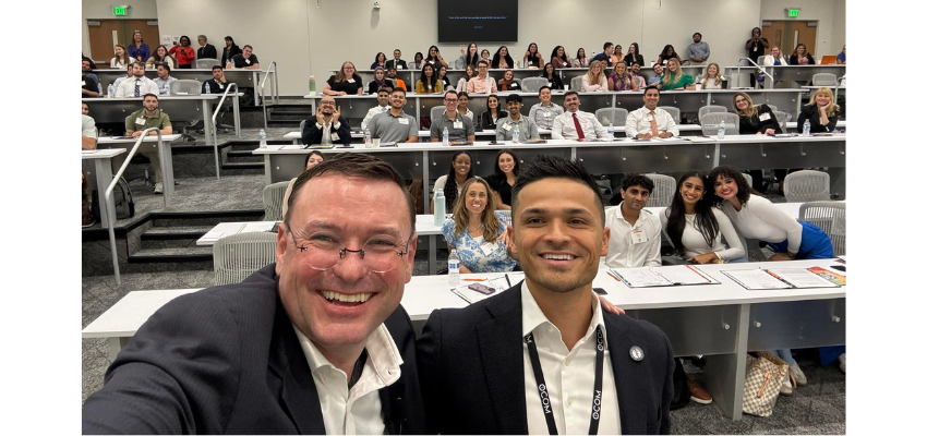 A large group of people in a lecture hall, with two individuals in the foreground taking a selfie.
