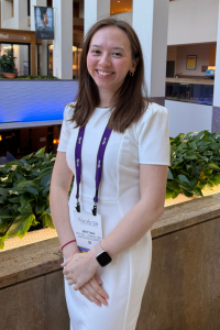 A medical student in professional attire, smiling while attending a conference.