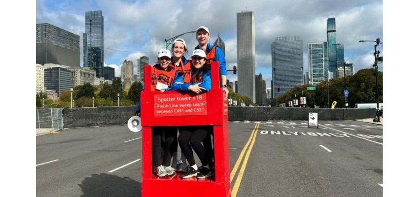 Volunteers standing on a red observation platform at a city marathon, with skyscrapers in the background.