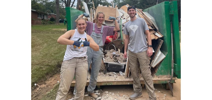 Students participate in a community service project, posing in front of a dumpster filled with construction debris.
