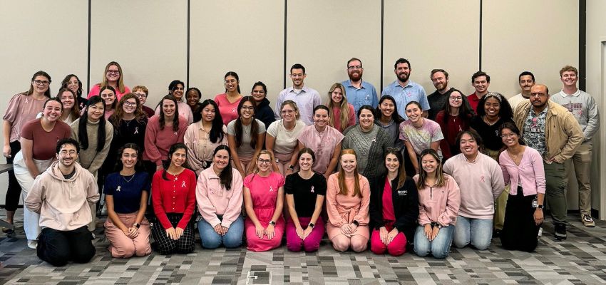 A large group of students and faculty pose together, many wearing pink in support of a cause.