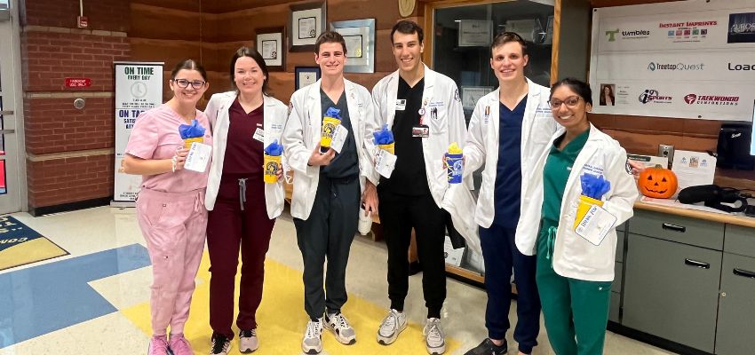 A group of medical students in white coats posing indoors, holding gifts, highlighting their engagement in a professional event or celebration.