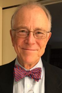 A headshot of an older individual wearing glasses and a bow tie, exuding professionalism and experience.