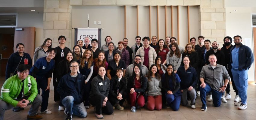 A large group of students and faculty pose together indoors for a group photo at a campus event.