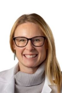 A woman wearing glasses and a white coat smiles in a professional headshot against a light background.