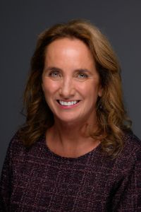 A woman smiles in a professional headshot against a dark background.