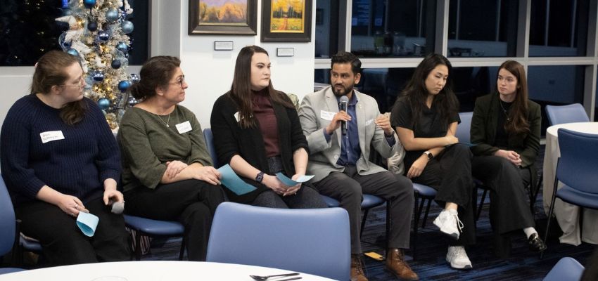 Panelists sit in a semi-circle during a moderated discussion, with one speaker holding a microphone while others listen.