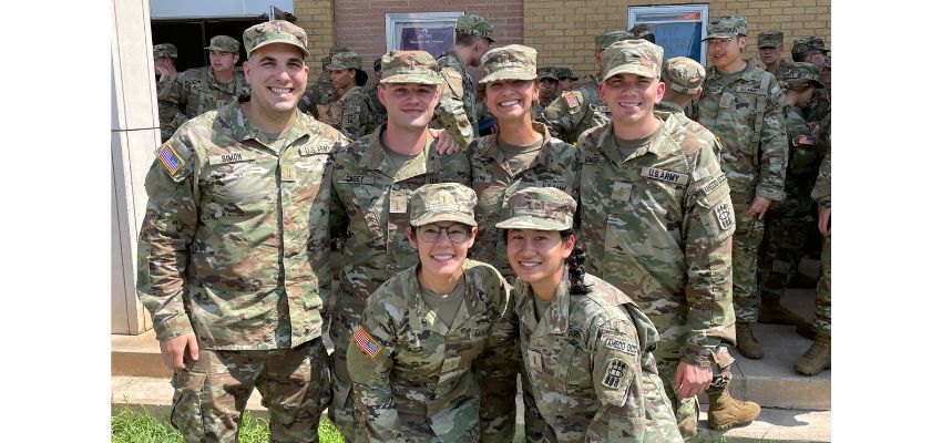 A group of uniformed service medical students smile together outdoors in front of a building.