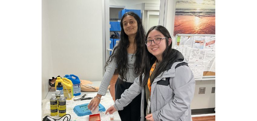 Two students smile while working together at a table with lab supplies during a classroom activity.